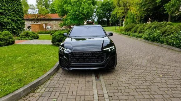 Czarne Audi Q8 stoi na brukowanej alejce w zielonym ogrodzie